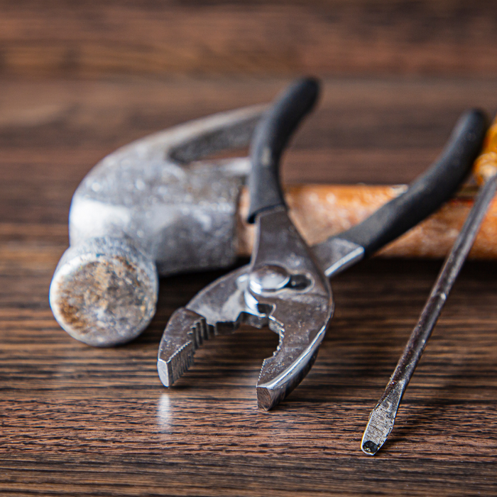 hammer, screwdriver and pliers laying against a wood backdrop