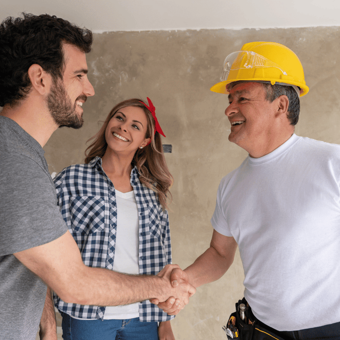 general contractor in a white t-shirt and yellow helmet shaking hands with a couple