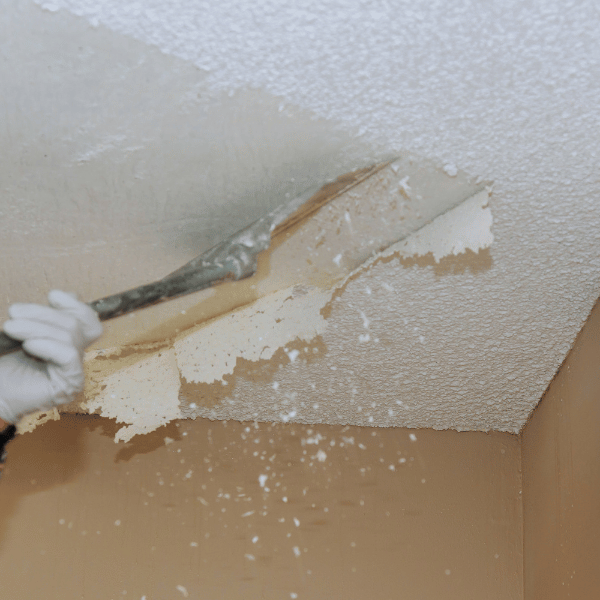 closeup of hands holding a scraper and removing a layer of popcorn texture ceiling