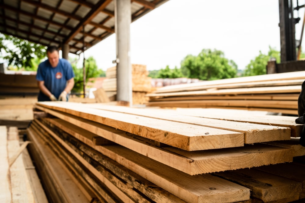 man out of focus stacking lumber in a yard